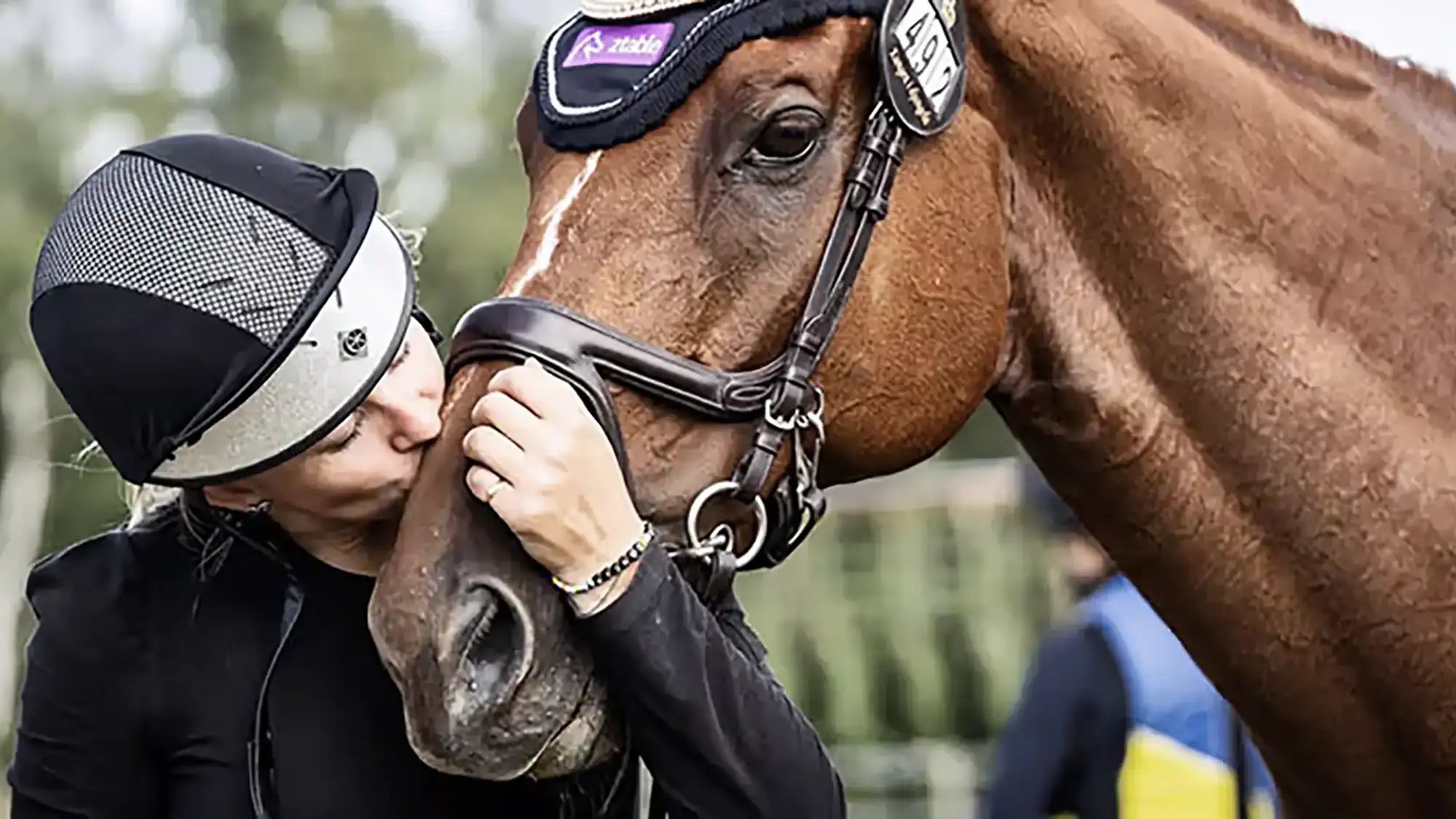 A rider kisses their horse on the muzzle.