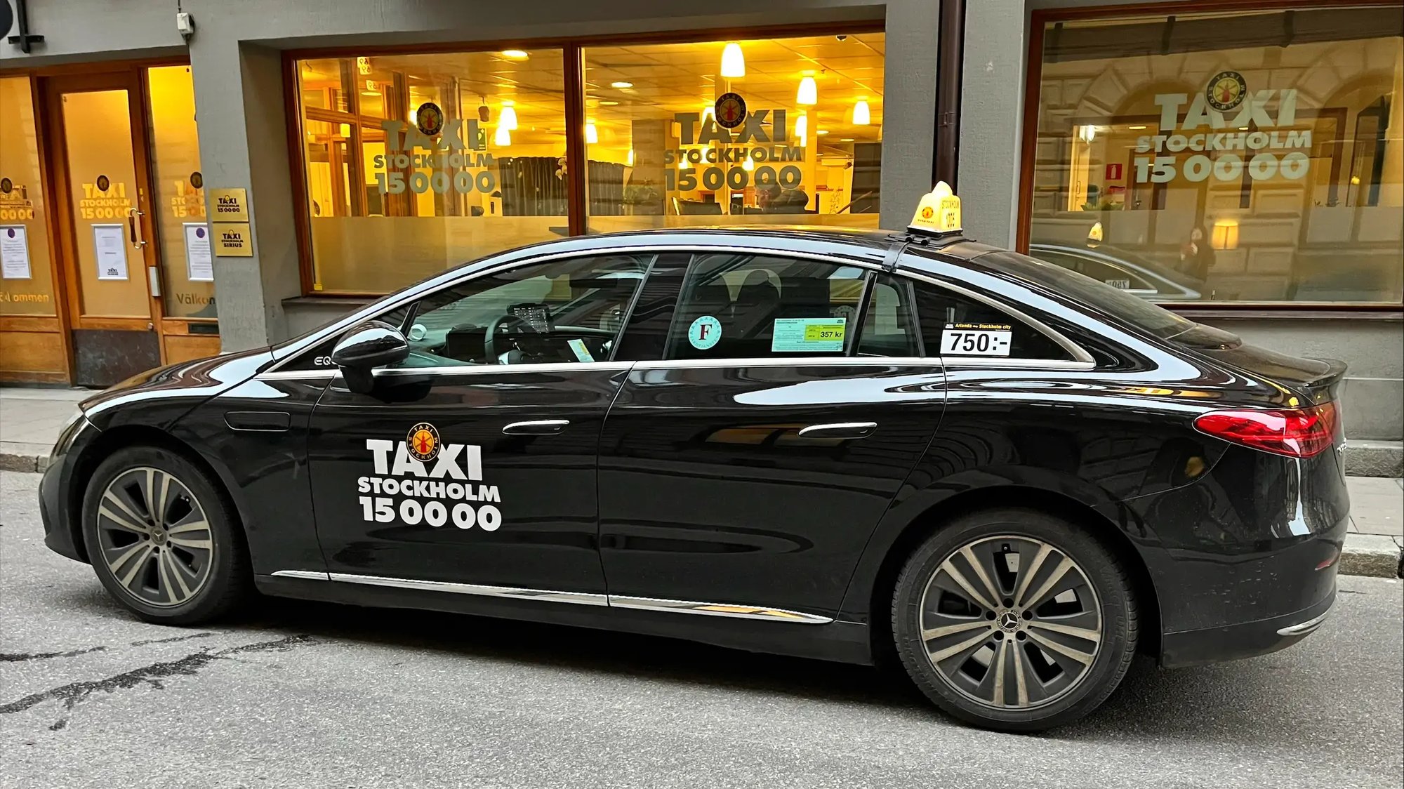 A Taxi Stockholm car in front of a shop window with the Taxi Stockholm logo.