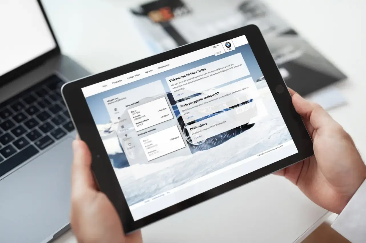 Händer som håller i en iPad, med BMW:s kundportal på skärmen