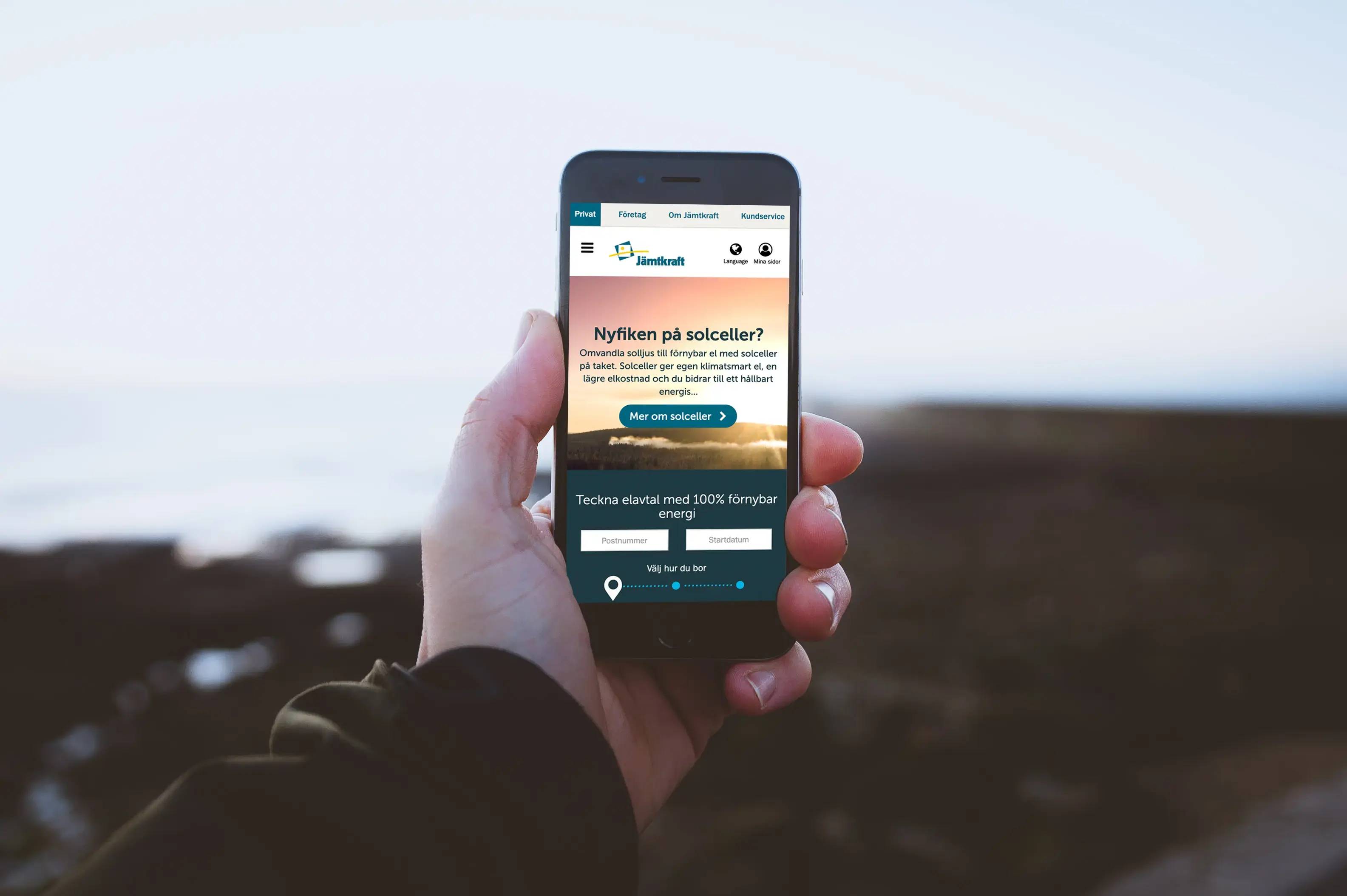 A hand holds a smartphone displaying Jämtkraft's website on the screen. In the background is the Jämtlandic nature.