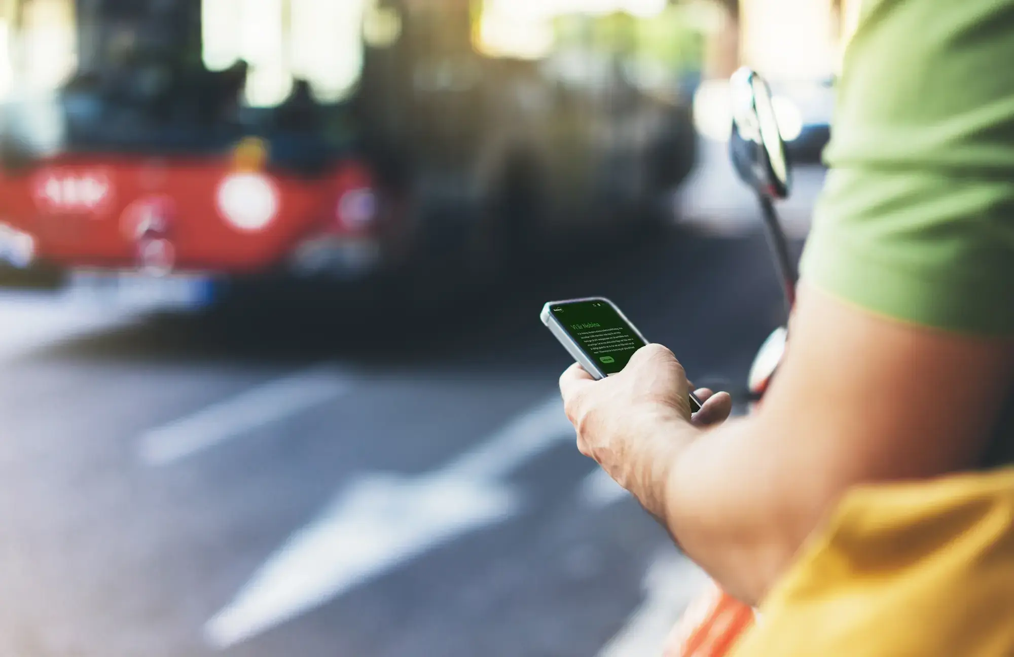 En person som tittar på sin smartphone med Nobinas webb på skärmen. I bakgrunden syns en röd buss i gatumiljö.