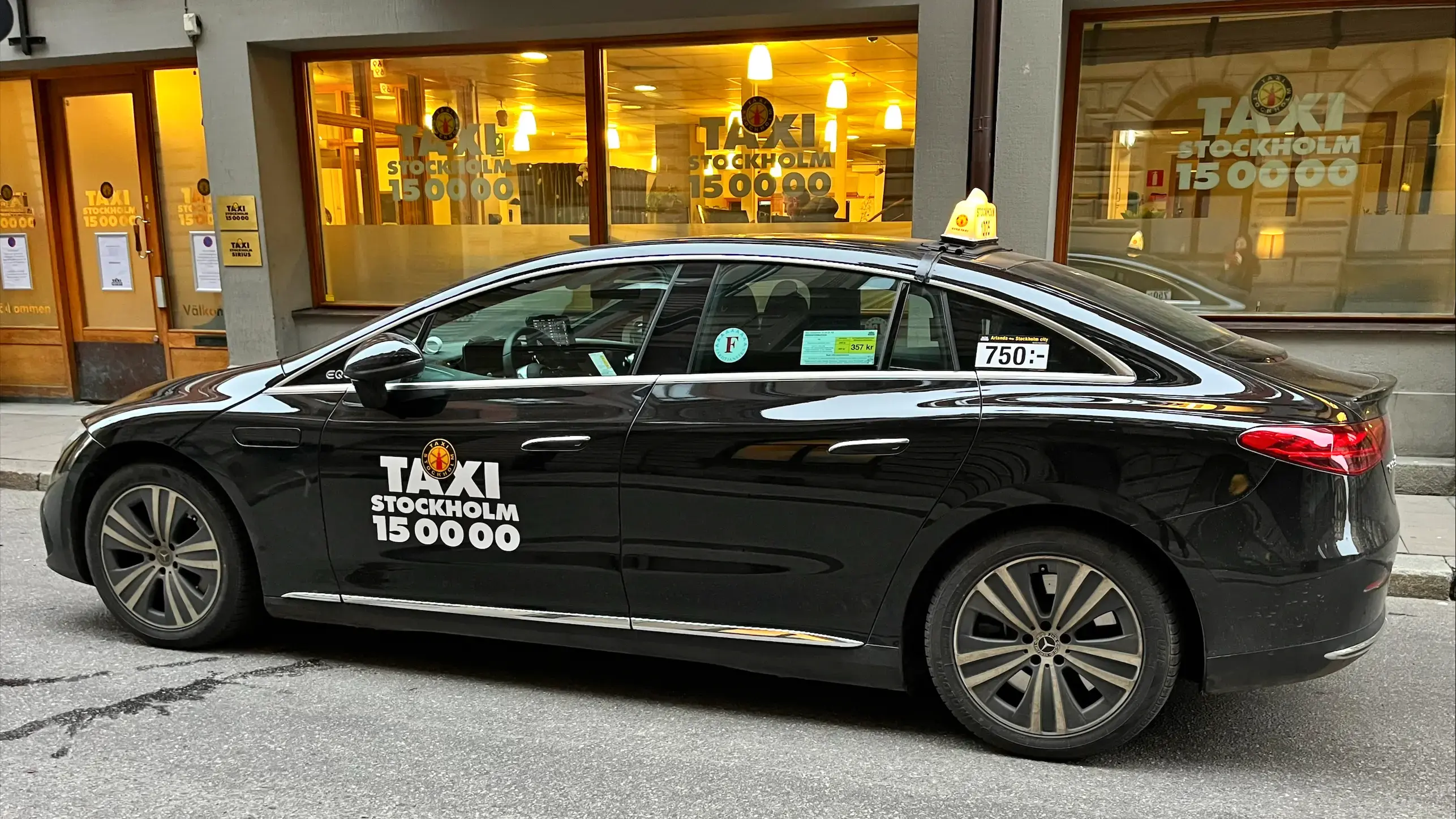 En Taxi Stockholm-bil framför ett skyltfönster med Taxi Stockholms logotyp.